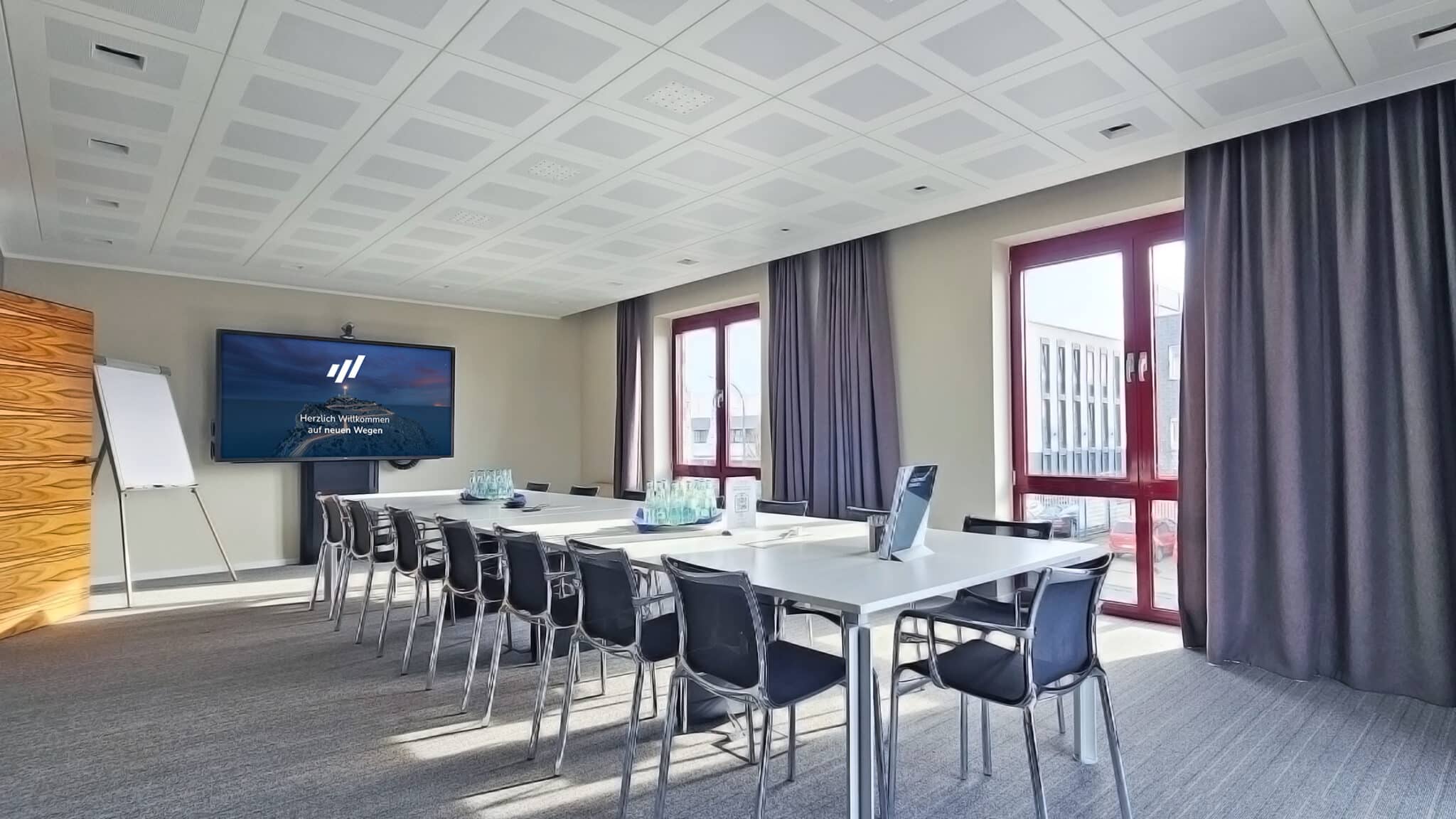 Konferenzraum mit einem langen Besprechungstisch und einem großen Bildschirm an der Wand.
