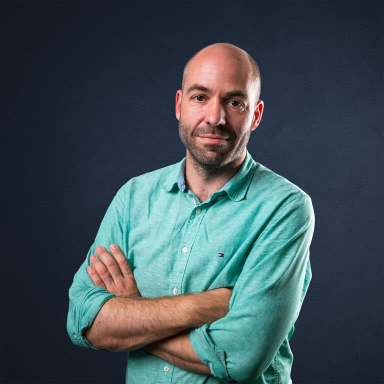 Porträt von Oliver Conrad mit verschränkten Armen, in einem hellgrünen Hemd vor dunklem Hintergrund.