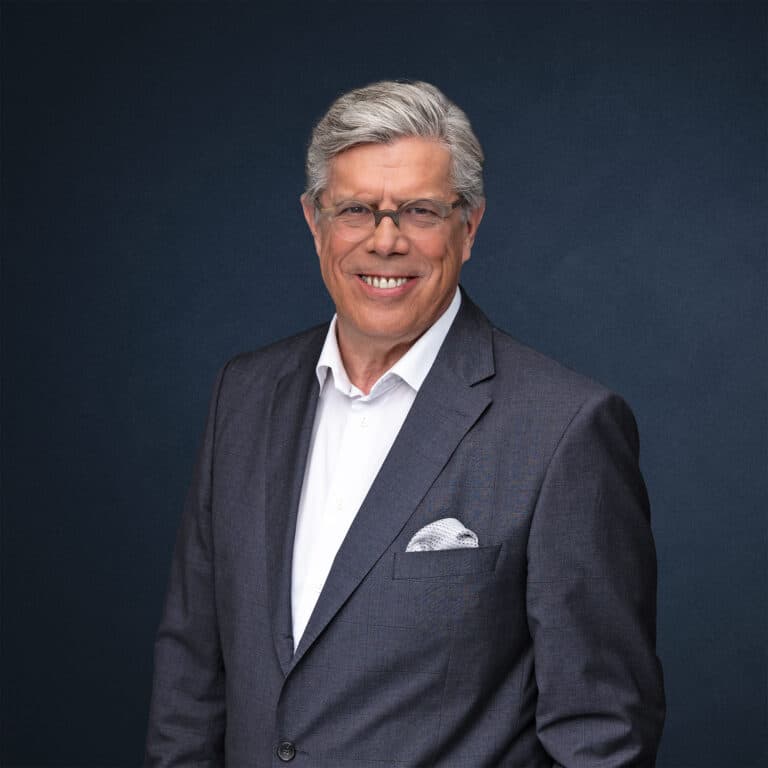 Porträt eines Mannes in einem Anzug mit grauem Hintergrund.